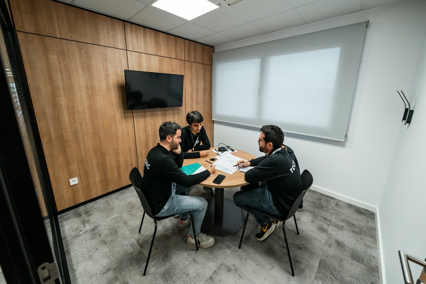 Three professionals discuss documents at a small meeting table.
