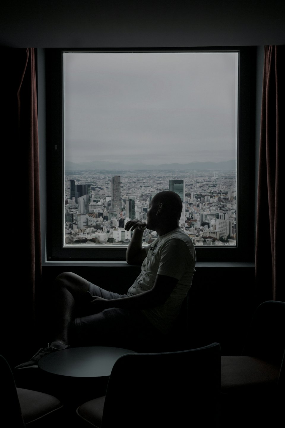 Man sits by a window looking out at a city skyline.