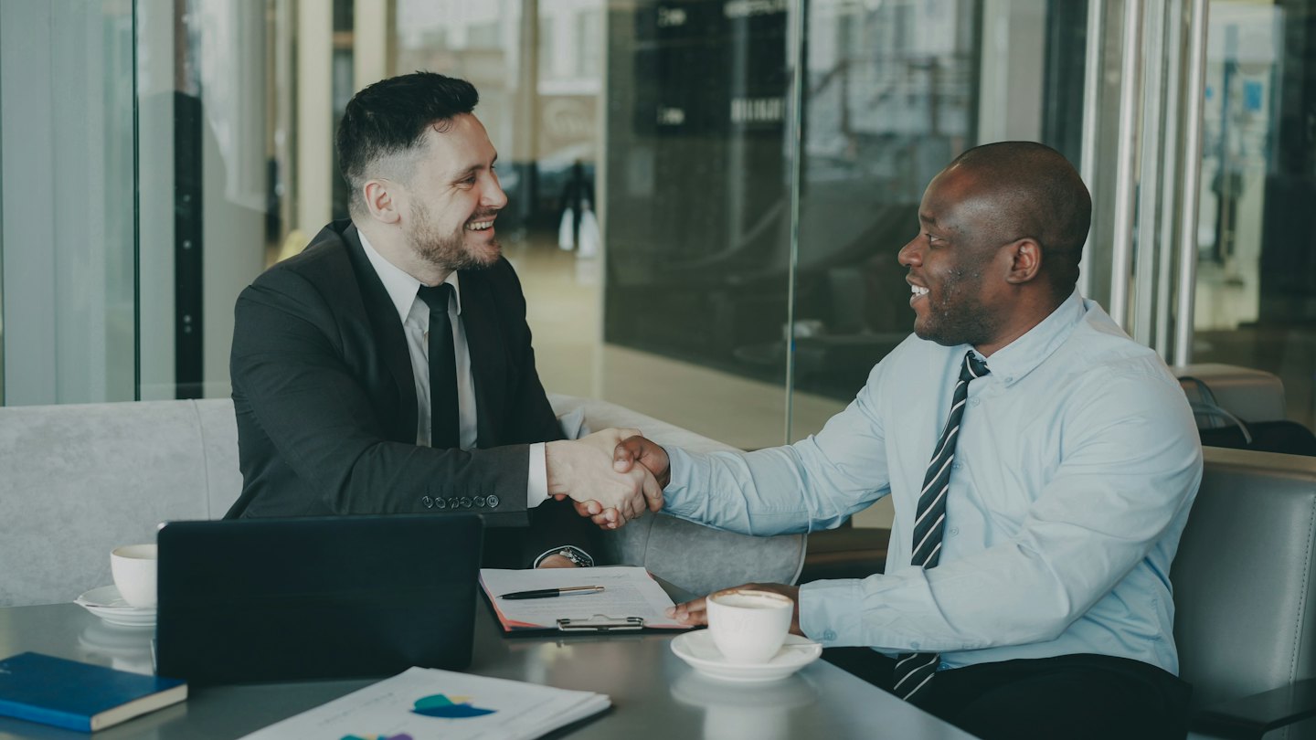 Two business professionals shake hands over a conference table.